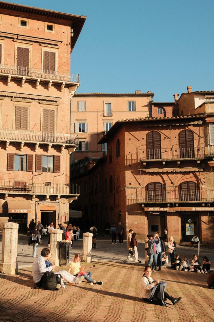 People enjoying a sunny afternoon in a Siena piazza with historic buildings.